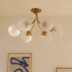 Clérachic six-head brass ceiling light seen unlit, its frosted herringbone-textured globes on curved arms beside framed art.