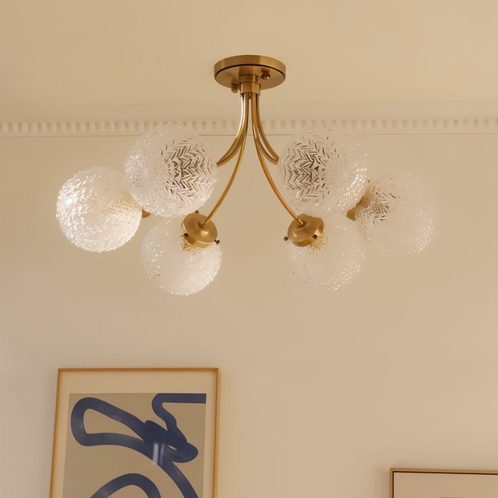 Clérachic six-head brass ceiling light seen unlit, its frosted herringbone-textured globes on curved arms beside framed art.