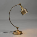 Side view of this Clérachic table lamp on grey, with the antique brass arm curving up to the angled shade and a warm glow on the base.