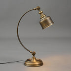 Side view of this Clérachic table lamp on grey, with the antique brass arm curving up to the angled shade and a warm glow on the base.