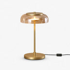 Clérachic table lamp on a white backdrop, an amber glass dome over a slim brass stem and round base, with an in-line switch on the black cord.
