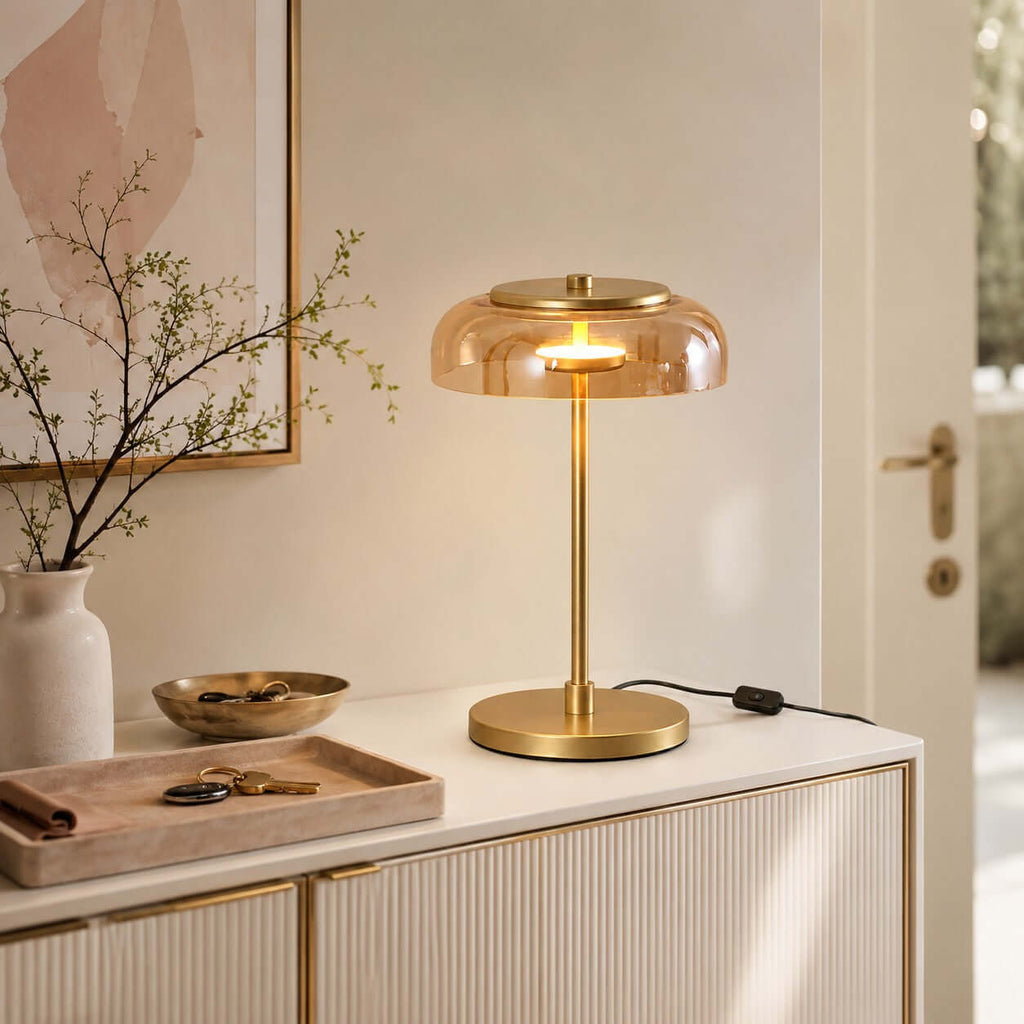 Clérachic amber-glass table lamp glowing on a white fluted cabinet, with a vase of branches and a small brass dish beside it.