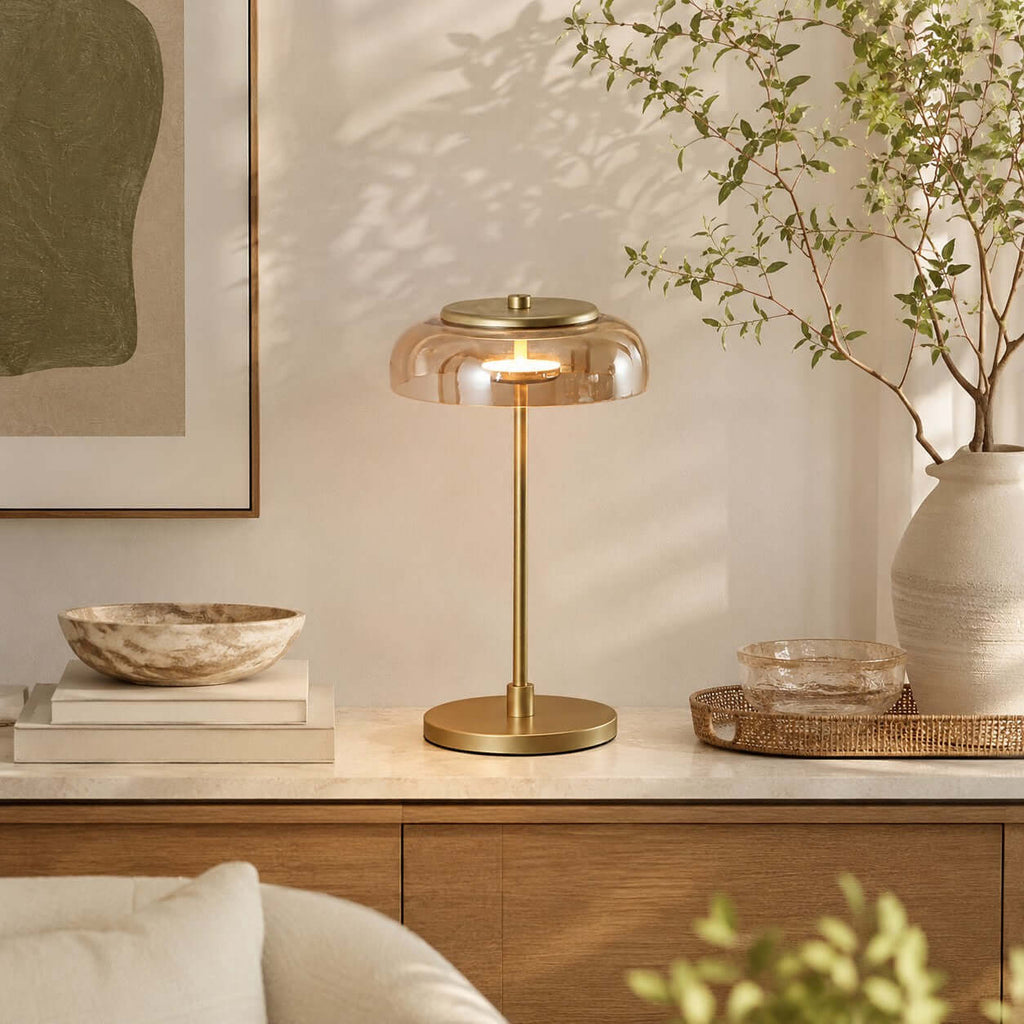 Amber-dome Clérachic table lamp lit on a marble-topped sideboard, with a stone bowl, stacked books and a large vase of branches.