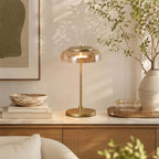Amber-dome Clérachic table lamp lit on a marble-topped sideboard, with a stone bowl, stacked books and a large vase of branches.