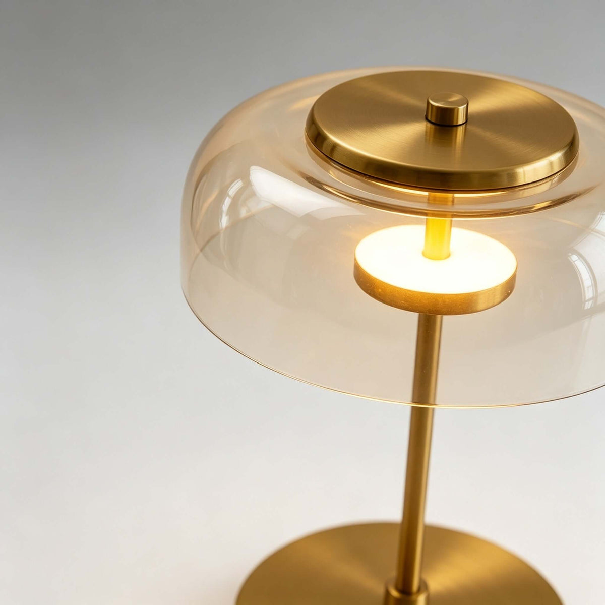 Close view of the amber glass dome, brushed brass cap and lit LED ring on this Clérachic table lamp.