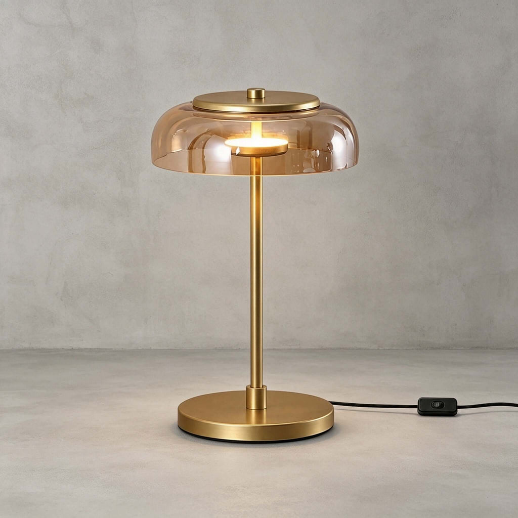 Clérachic table lamp with an amber glass dome on a grey backdrop, its brass stem and round base standing on a pale floor.