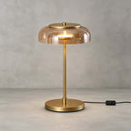 Clérachic table lamp with an amber glass dome on a grey backdrop, its brass stem and round base standing on a pale floor.