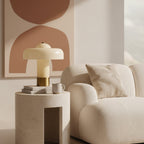 A Clérachic cream mushroom-shaped lamp on a stone side table, with a mug and books, beside a cream boucle armchair.