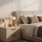 On a cream bedside chest with brass handles, this Clérachic lamp stands beside a small vase and a brass alarm clock.