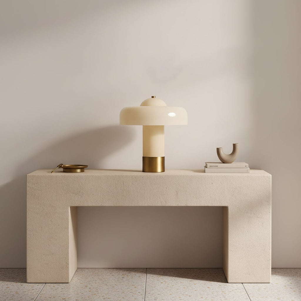 A Clérachic cream and brass table lamp on a pale stone console, with a small brass dish and a sculptural ornament.