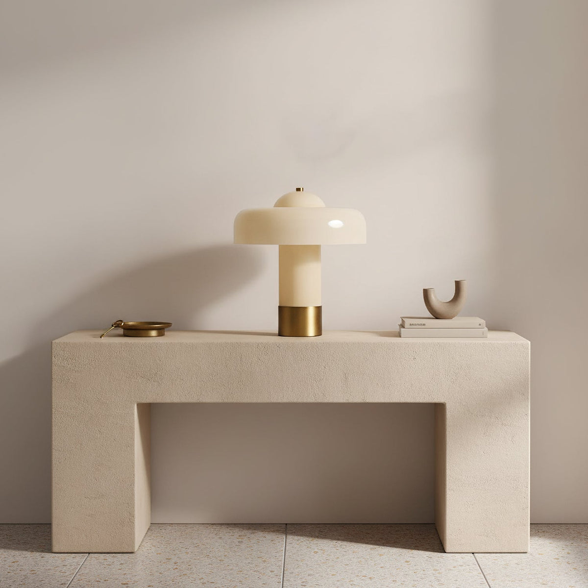 A Clérachic cream and brass table lamp on a pale stone console, with a small brass dish and a sculptural ornament.