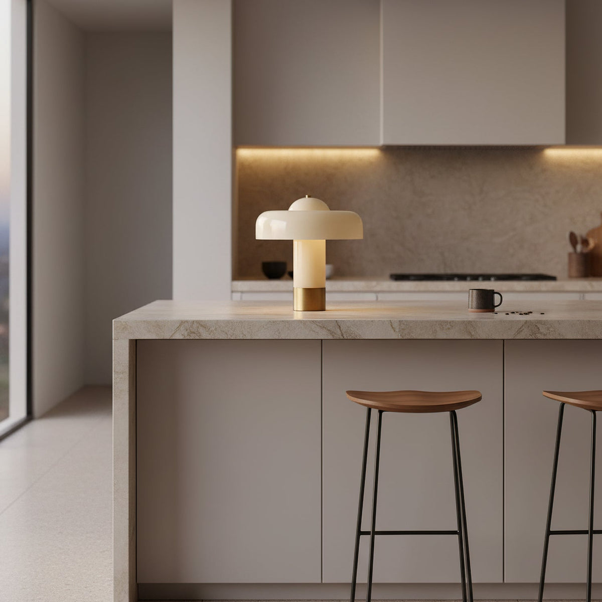 A small Clérachic cream lamp with a brass base on a marble kitchen island, with wooden bar stools below.