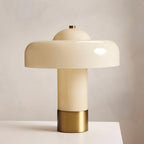 Close view of the glossy cream shade, stem and brass collar of this Clérachic table lamp, on a pale surface.