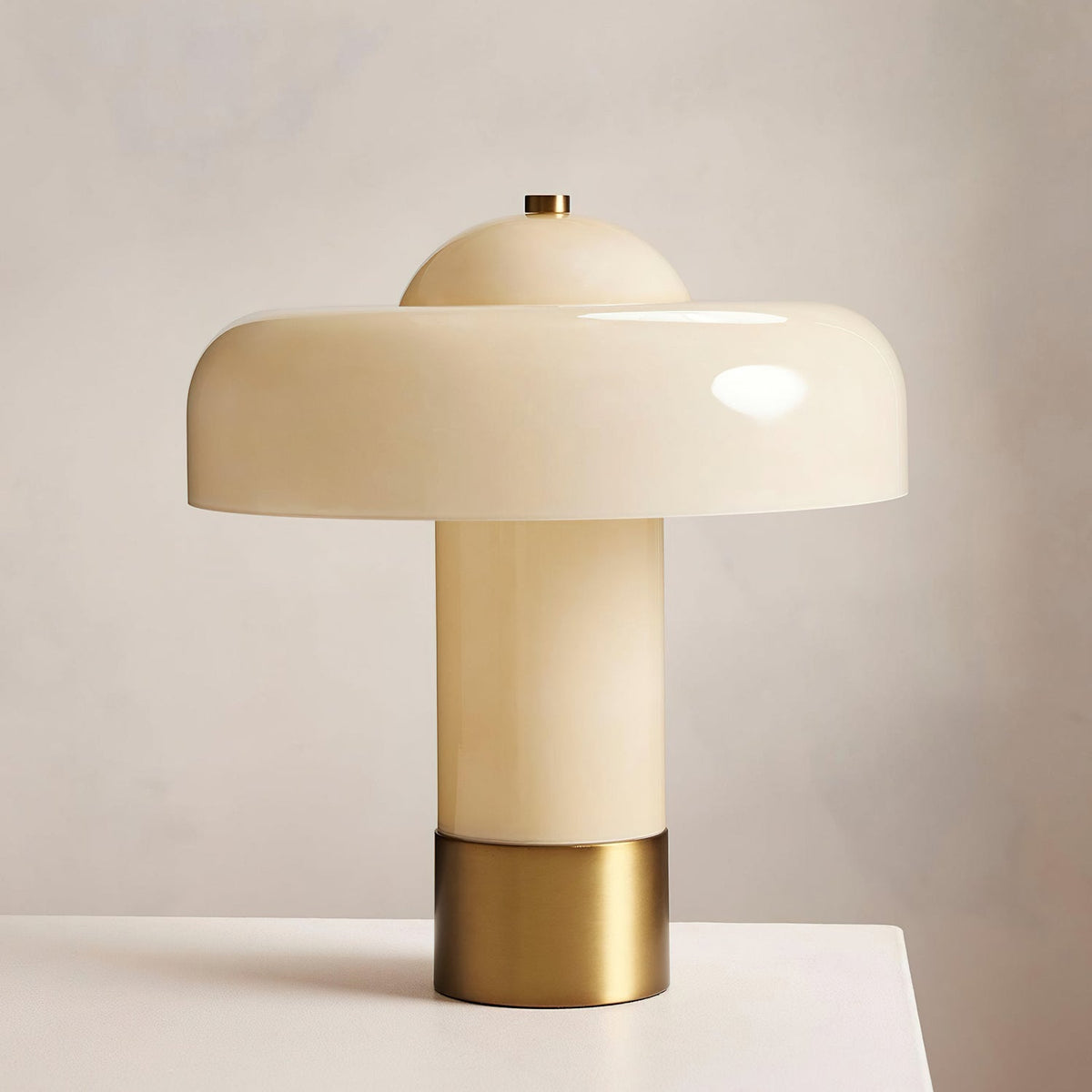 Close view of the glossy cream shade, stem and brass collar of this Clérachic table lamp, on a pale surface.
