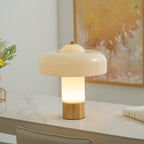 The stem of this Clérachic table lamp glows warm white under its cream shade, on a white marble desk by a golden painting.