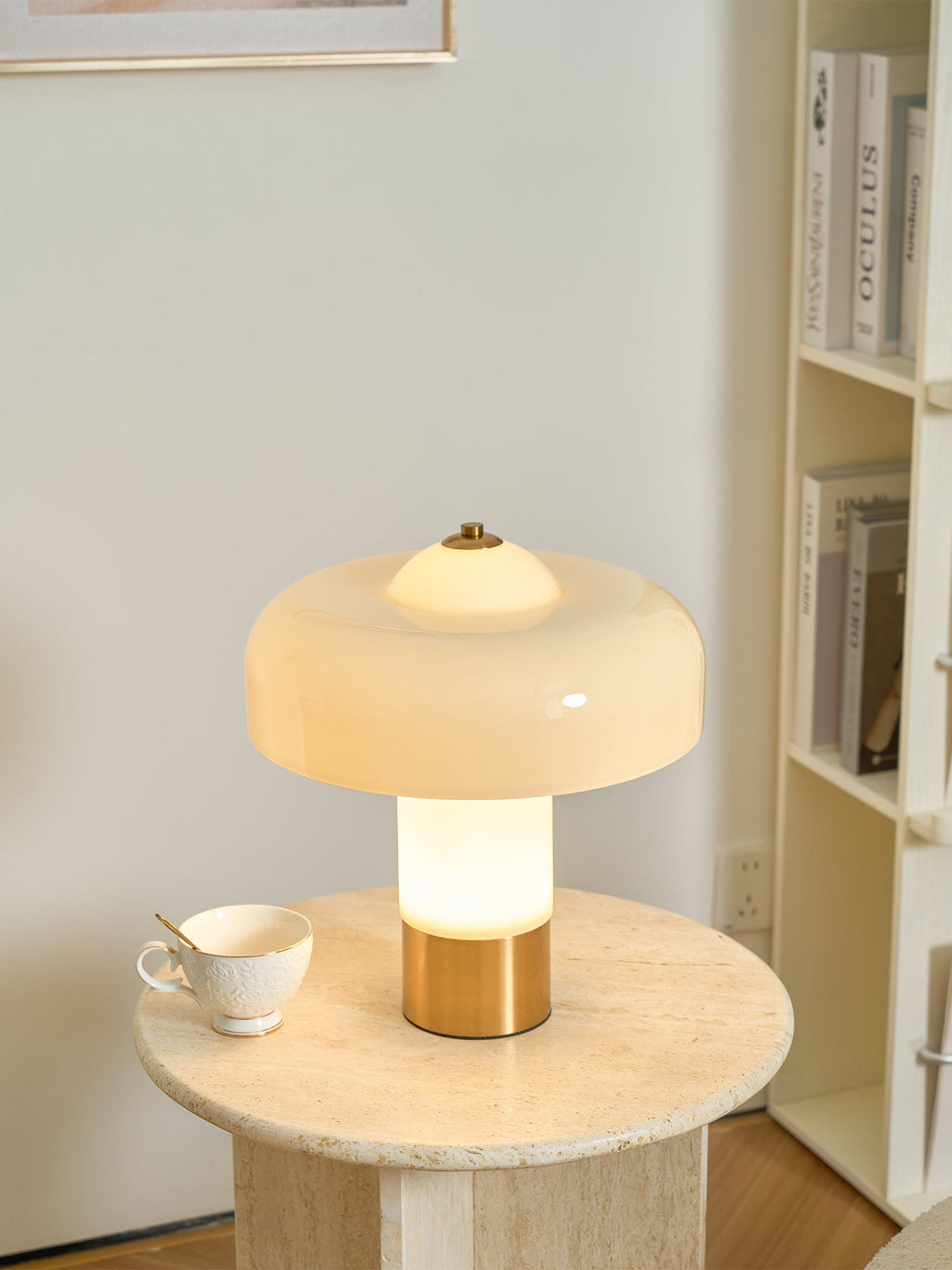 From a slightly nearer view, the lit stem of this Clérachic cream lamp glows warm above its brass base, with a teacup on the table.
