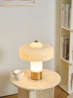 From a slightly nearer view, the lit stem of this Clérachic cream lamp glows warm above its brass base, with a teacup on the table.