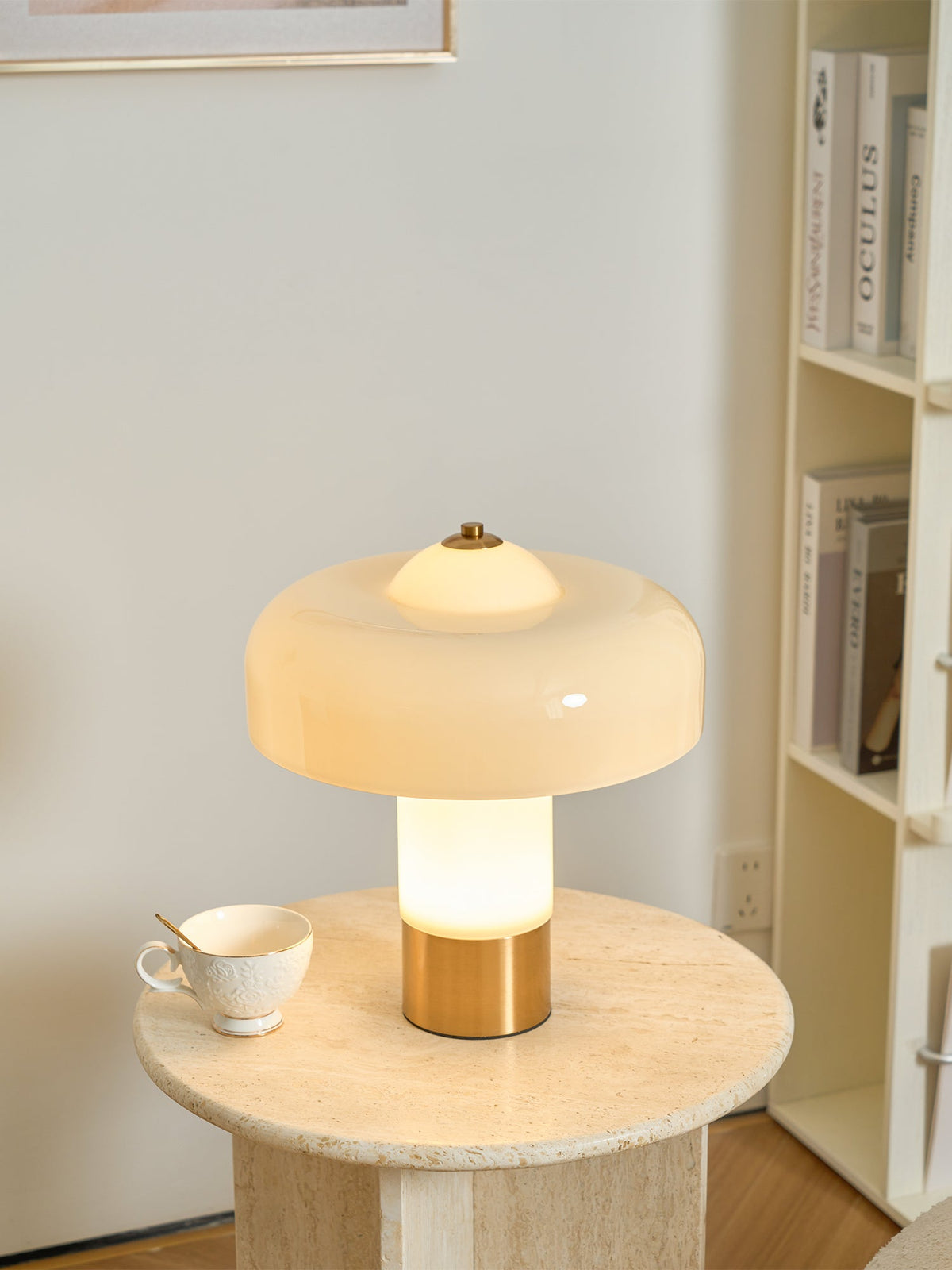 From a slightly nearer view, the lit stem of this Clérachic cream lamp glows warm above its brass base, with a teacup on the table.