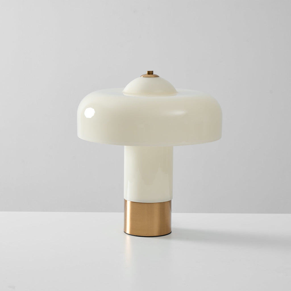 Front view of an unlit Clérachic table lamp with a glossy cream shade, a cream stem and a brass base, on a pale grey surface.
