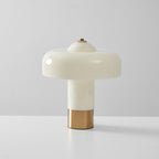 Front view of an unlit Clérachic table lamp with a glossy cream shade, a cream stem and a brass base, on a pale grey surface.