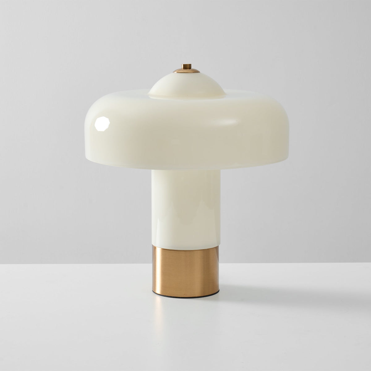 Unlit Clérachic table lamp with its glossy cream shade and brass collar, seen head-on against a pale grey wall.