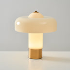 The Clérachic cream lamp with its stem lit warm and a soft glow around the brass base, on a pale grey surface.