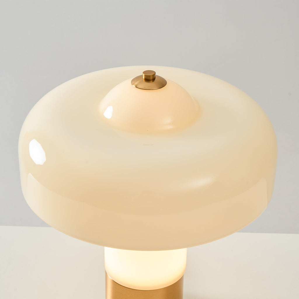 Close view of the glossy cream shade and small brass cap on top of this Clérachic table lamp, with its lit stem below.