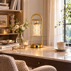 Clérachic table lamp on a marble desk by a window with sheer curtains, next to a cup and saucer and a posy of white flowers.