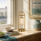 Clérachic table lamp on a wooden console by a window with a city view, beside a green vase and a stack of magazines.