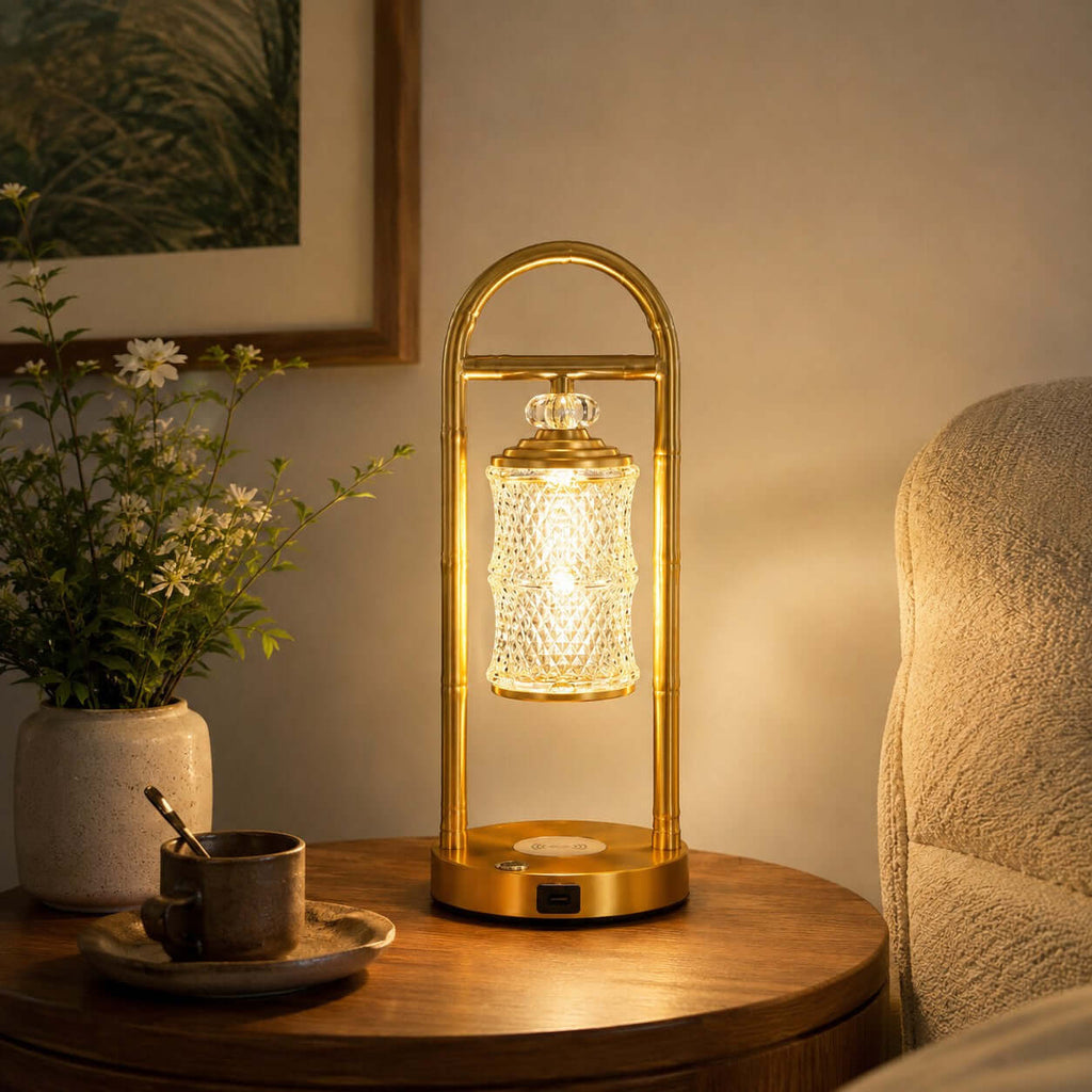 Warmly lit Clérachic table lamp on a round wooden table, with a ceramic cup and spoon and a vase of daisies beside it.
