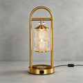 Brass Clérachic table lamp on a grey concrete-look backdrop, its black cord and in-line switch trailing to the right.