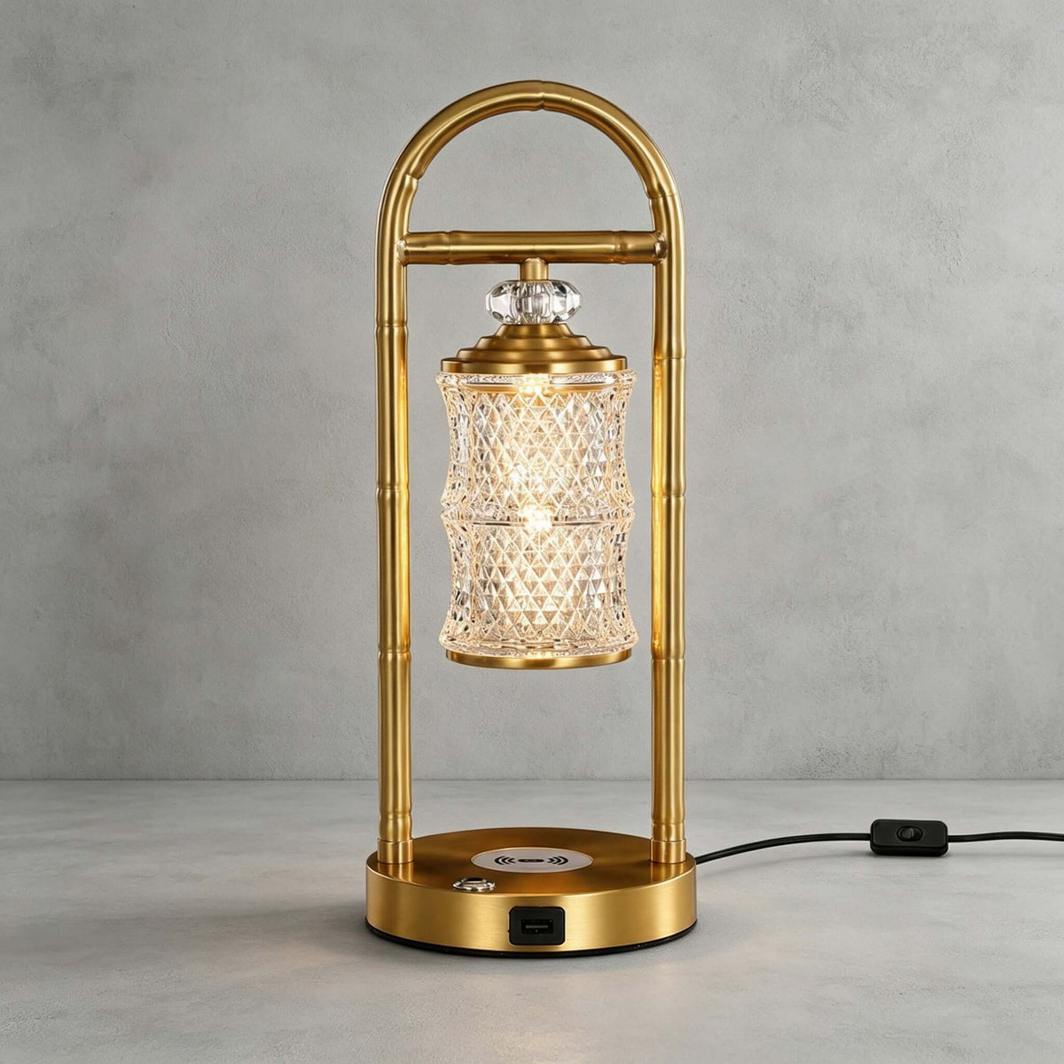 Brass Clérachic table lamp on a grey concrete-look backdrop, its black cord and in-line switch trailing to the right.