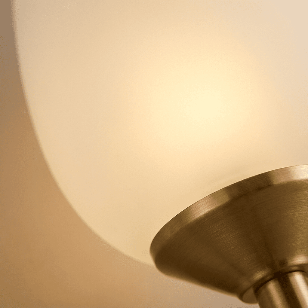 Close-up of the Clérachic frosted glass shade glowing softly above its brushed brass cup, with the stem just in view.