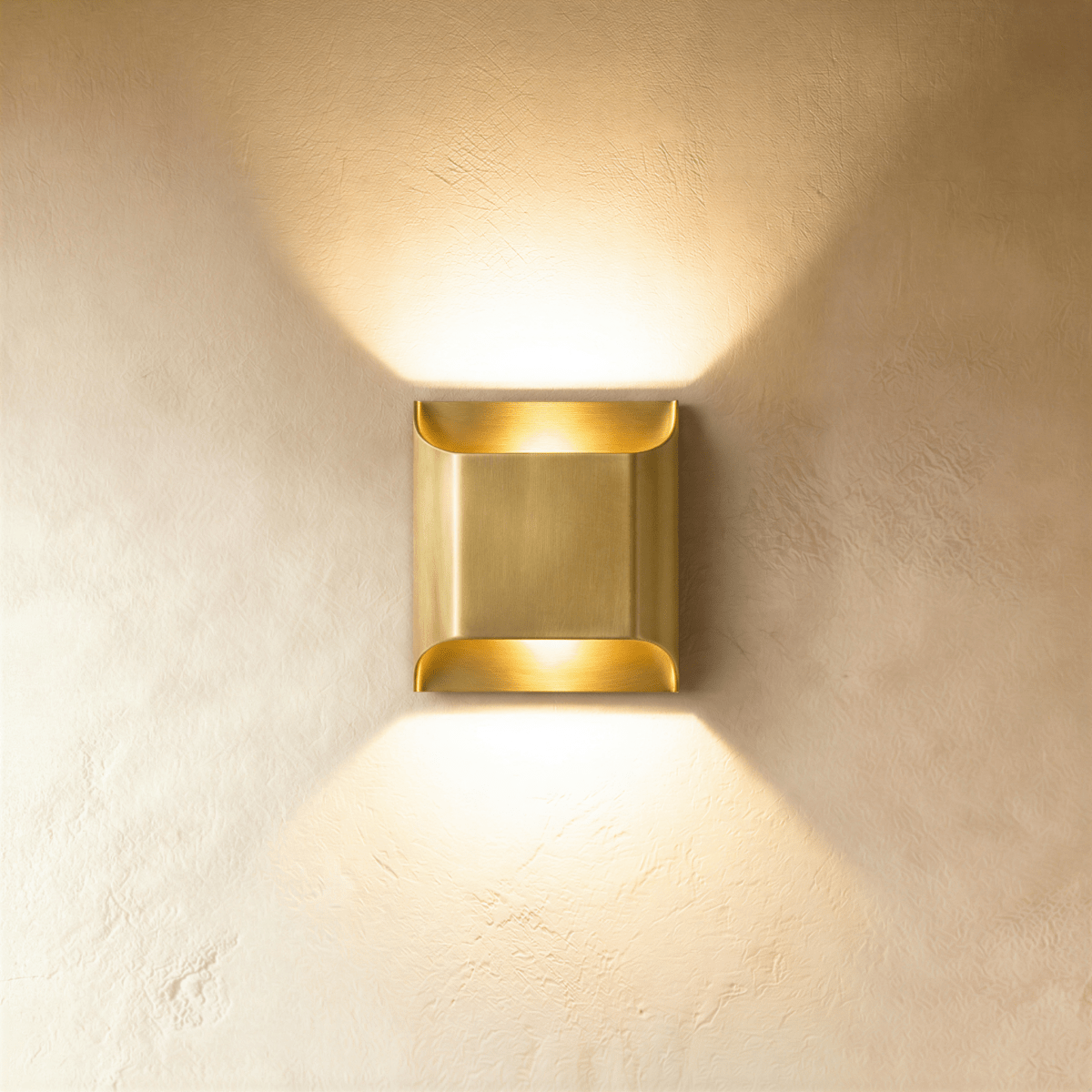 Clérachic antiqued brass wall light with curved edges, throwing warm light up and down a limewash wall.