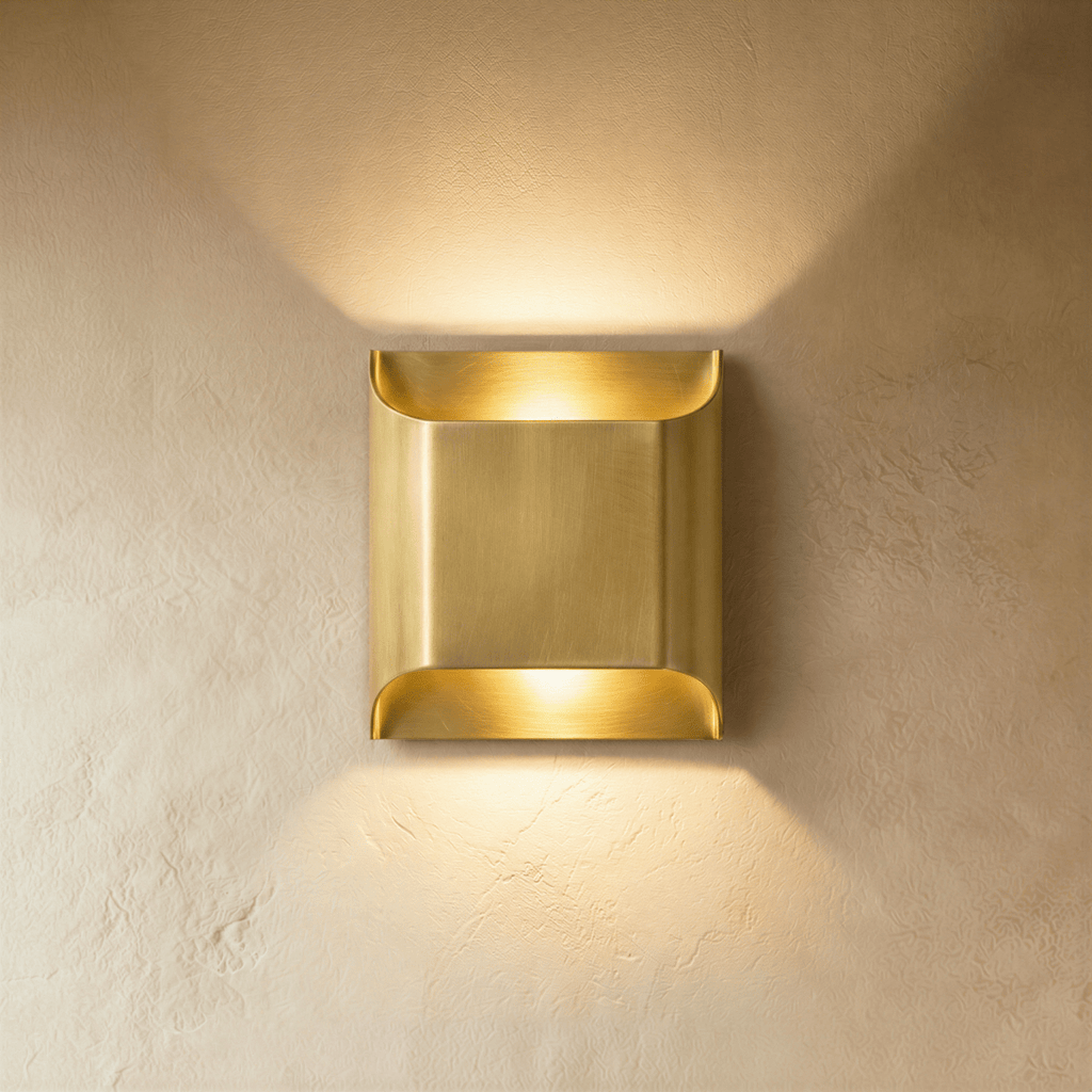 Clérachic mid-size brushed brass wall light, its curved lips casting warm light up and down a plaster wall.