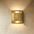 Clérachic mid-size brushed brass wall light, its curved lips casting warm light up and down a plaster wall.