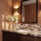 Clérachic square brass wall light beside a mirror above a marble vanity in a warm terracotta-toned bathroom.