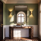 Pair of Clérachic tall brass wall lights flanking a gilt mirror above a marble console in a green-walled hall.
