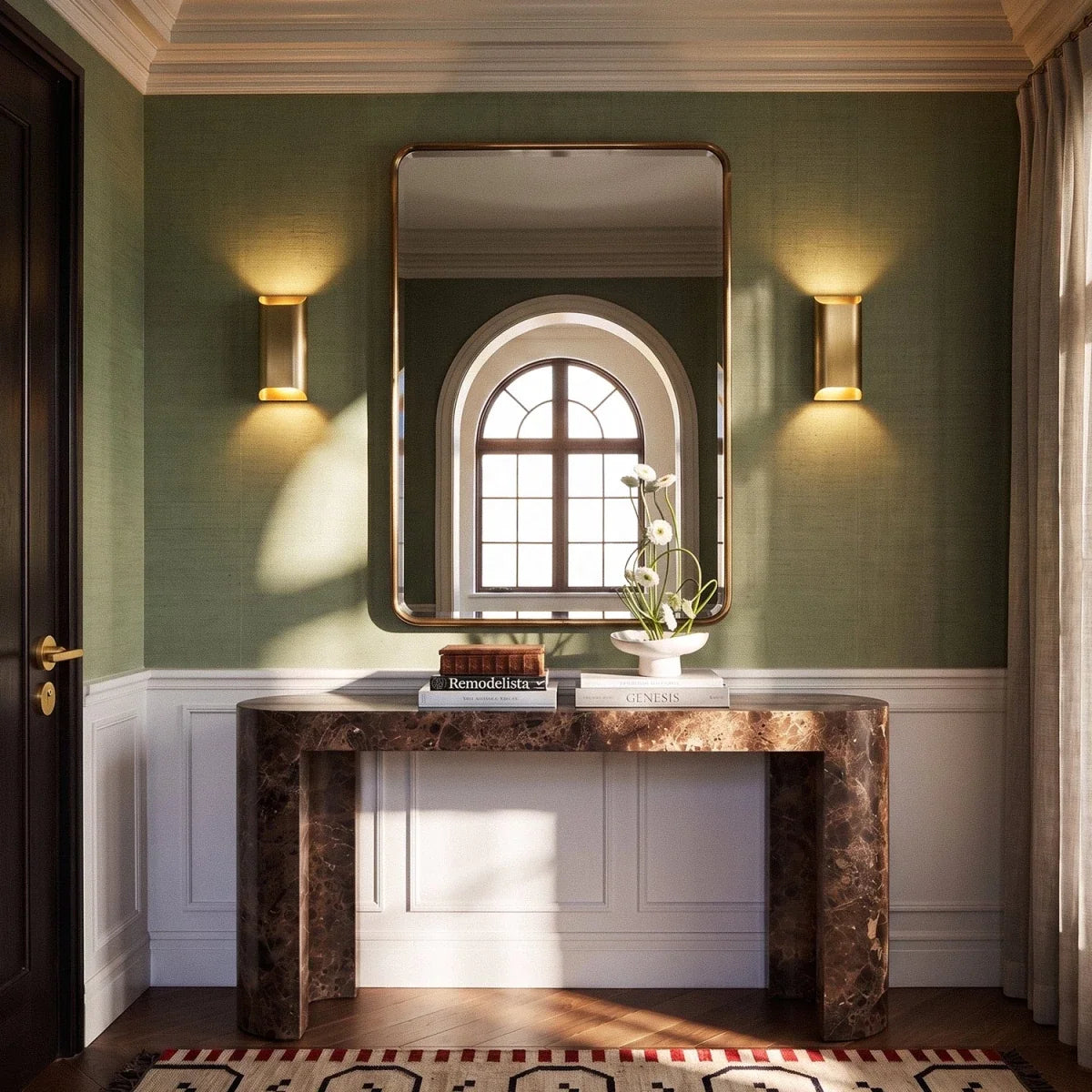 Pair of Clérachic tall brass wall lights flanking a gilt mirror above a marble console in a green-walled hall.