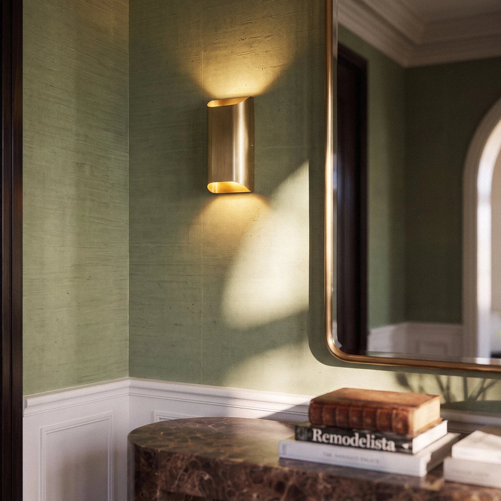 Clérachic tall brass wall light on green grasscloth wallpaper above a marble console with stacked books.