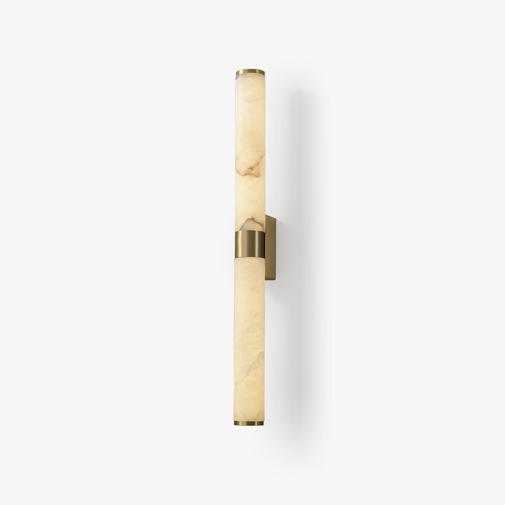 A tall alabaster tube wall light on a plain white backdrop, with a brass band at the middle and a small brass wall plate, from Clérachic.