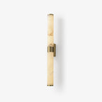 A tall alabaster tube wall light on a plain white backdrop, with a brass band at the middle and a small brass wall plate, from Clérachic.
