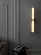 A single alabaster tube with a brass band glows on a charcoal panelled wall above a small black side table, from Clérachic.