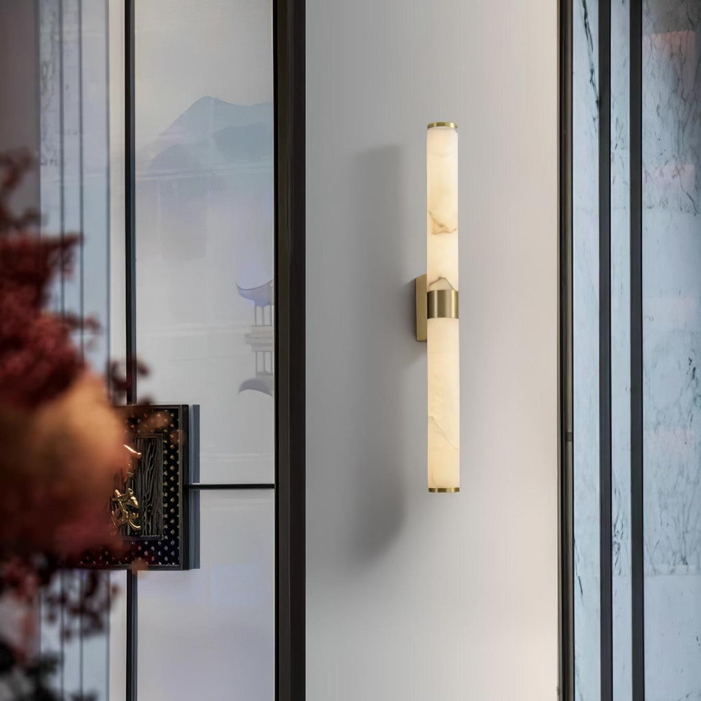At a glass partition with a painted landscape panel, a Clérachic alabaster tube wall light with a brass band hangs on a pale wall.