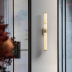 At a glass partition with a painted landscape panel, a Clérachic alabaster tube wall light with a brass band hangs on a pale wall.