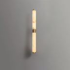 A narrower view of this Clérachic wall light on a grey wall, with alabaster veining, brass end caps and a casting shadow.