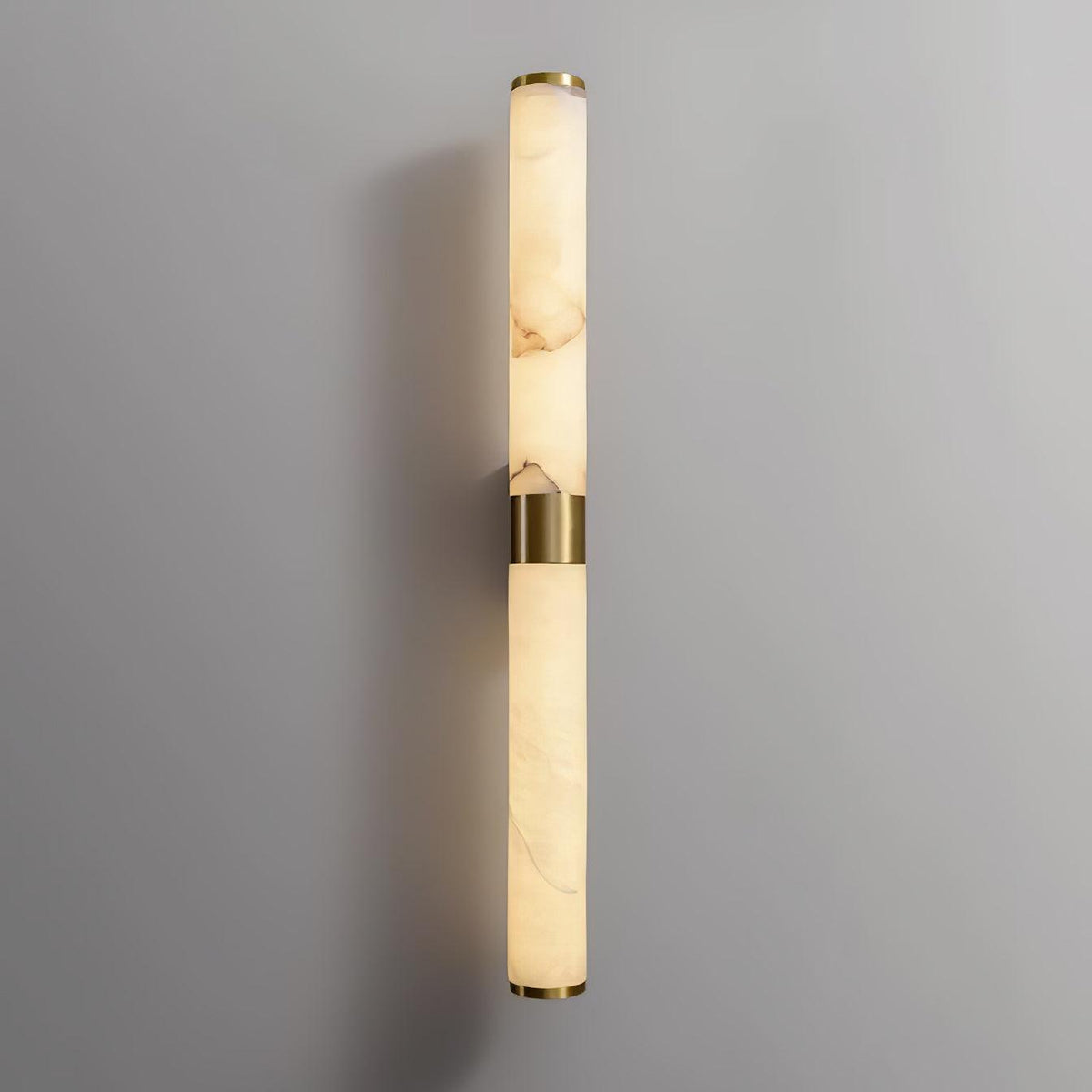 Straight on, the brass band and two veined alabaster tubes of this Clérachic wall light glow warm against a light grey wall.