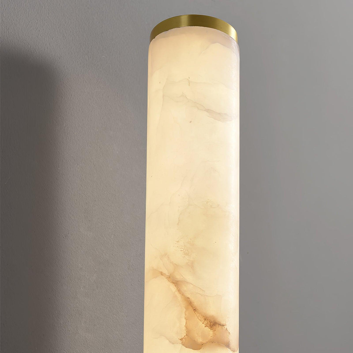 Close view of the top of a Clérachic alabaster tube, with its soft cream and tan veining and a thin brass end cap.