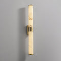 A tall alabaster tube with a brass band on a grey wall, with its brass back plate showing behind the band, from Clérachic.