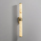 A tall alabaster tube with a brass band on a grey wall, with its brass back plate showing behind the band, from Clérachic.